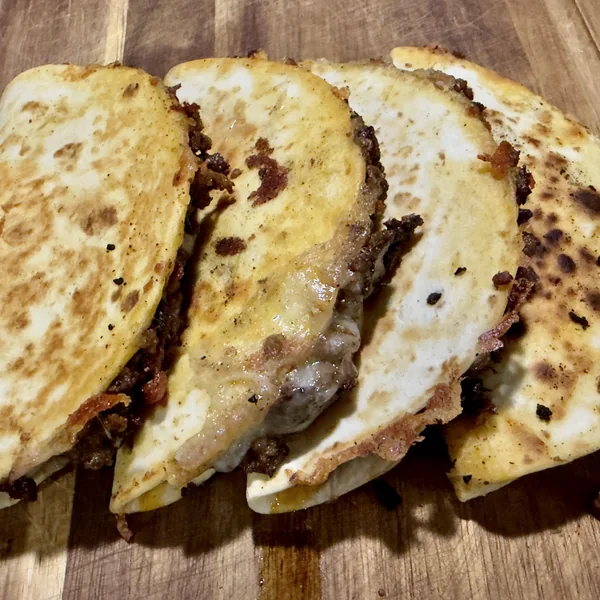 Folded skillet-crisped sausage tacos on a cutting board with melted Oaxaca cheese showing between the tortillas