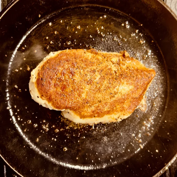 Overhead photo of the golden-brown chicken crust in cast iron immediately after flipping and before basting