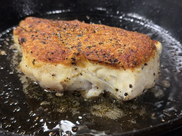 Side-angle photo of a browned chicken breast just after flipping, before the butter baste